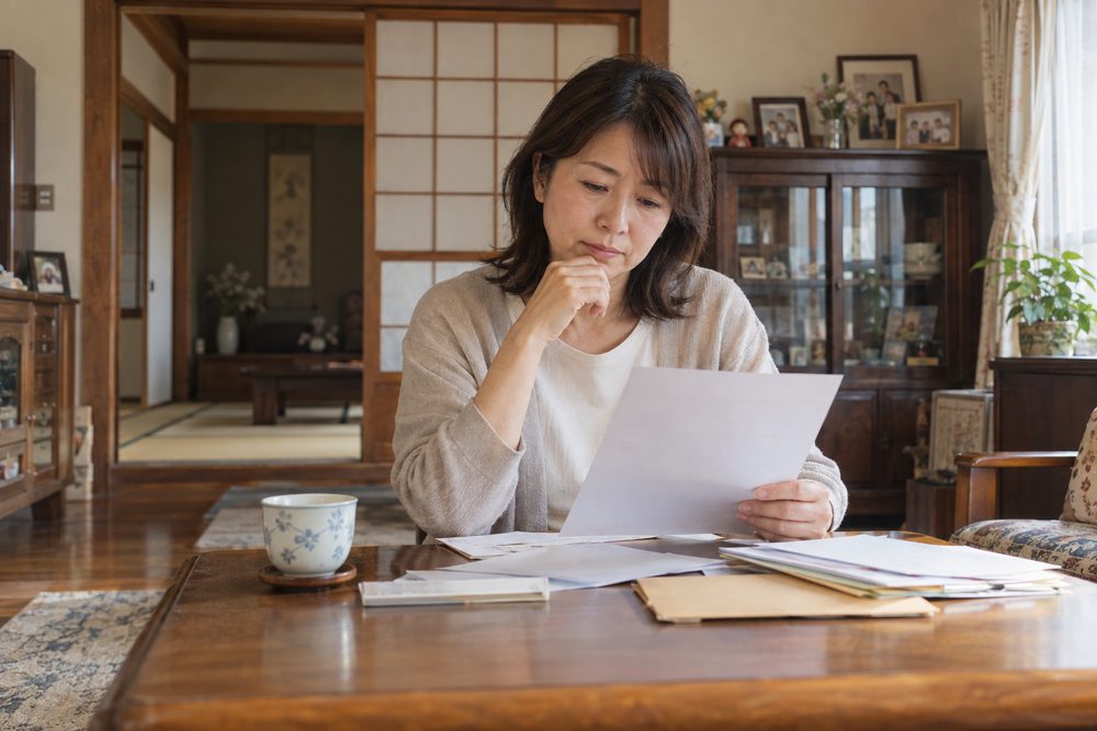 実家の居間で書類を前に考える女性のイメージ